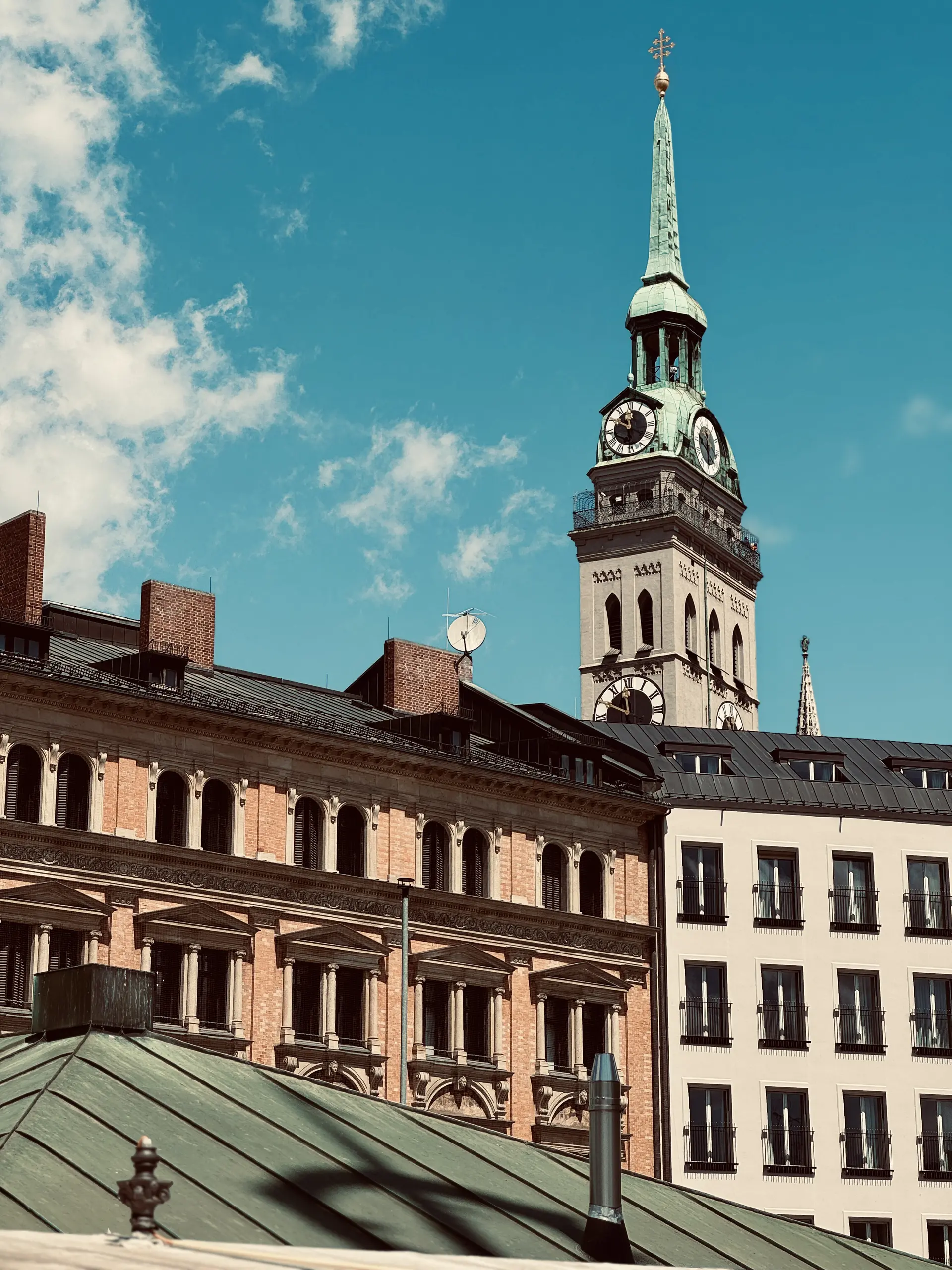 The clock tower of St. Peter's Church in Munich against a bright blue sky.