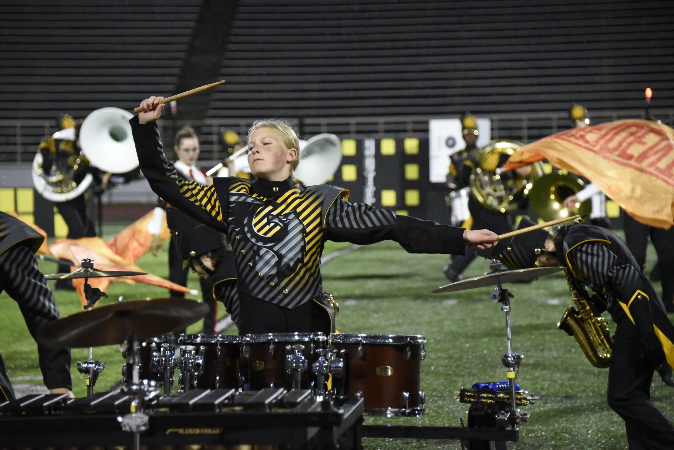 Molly Boon, age 9, drumming in the rain at a marching band competition, arms swung mid-rhythm.