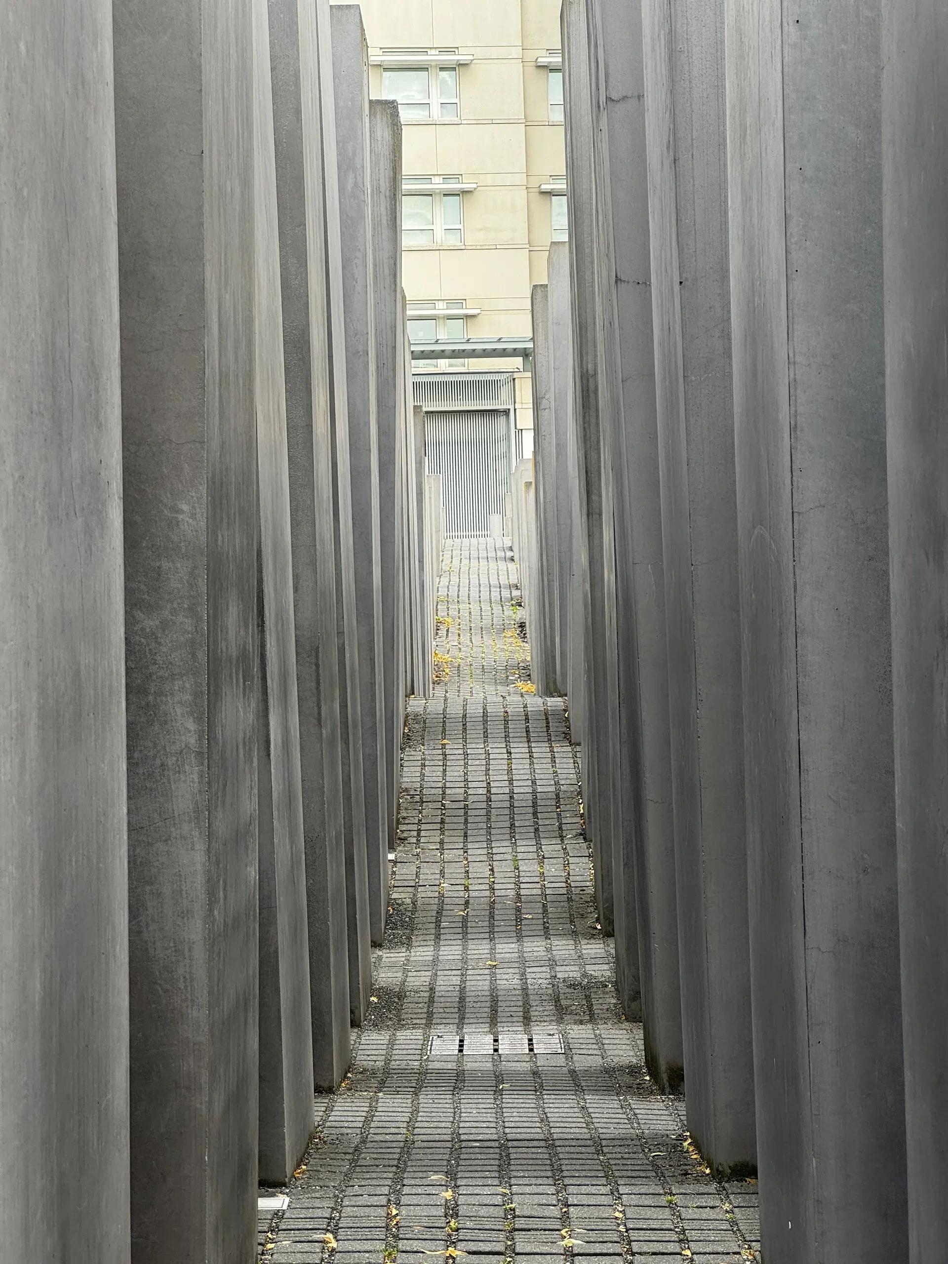 A narrow pathway between tall gray concrete slabs at the Memorial to the Murdered Jews of Europe in Berlin.